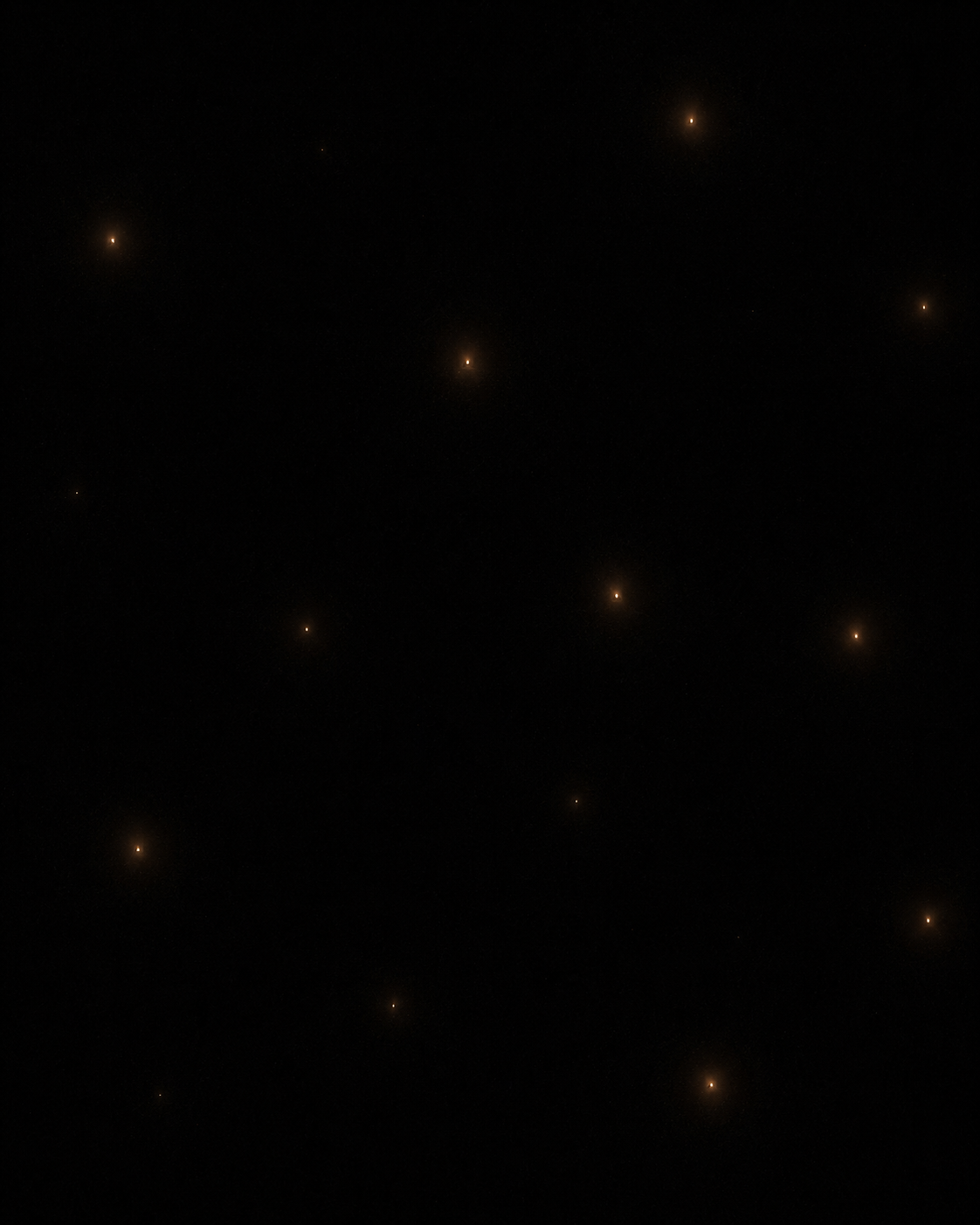 Scattered points of warm light against total blackness, each glowing alone in its own small halo, none close to another.